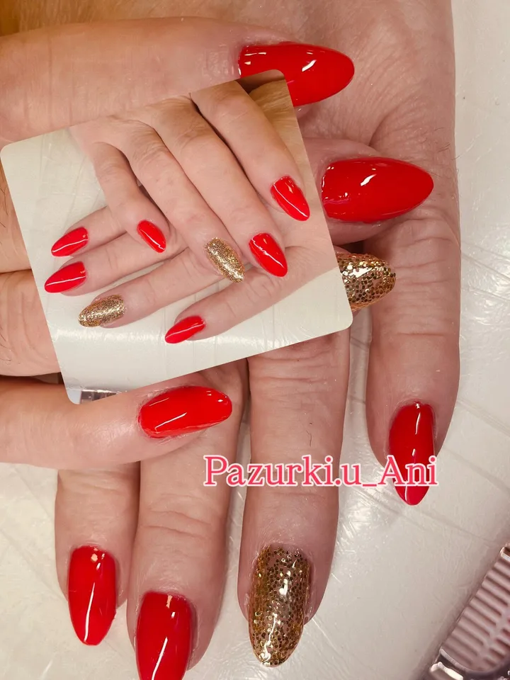 Czerwony manicure na paznokciach w kształcie migdałów ze złotym brokatem na wybranych paznokciach.